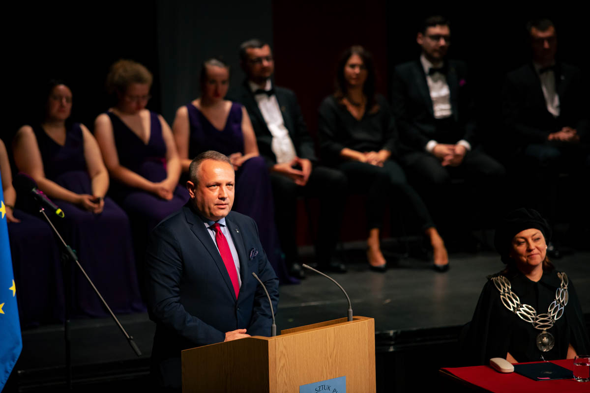 Mężczyzna na mównicy. Osoby na widowni w tle