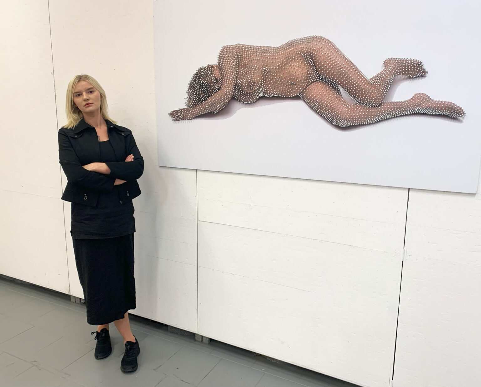 Kobieta stojąca obok swojej pracy, wyeksponowanej na ścianie galerii