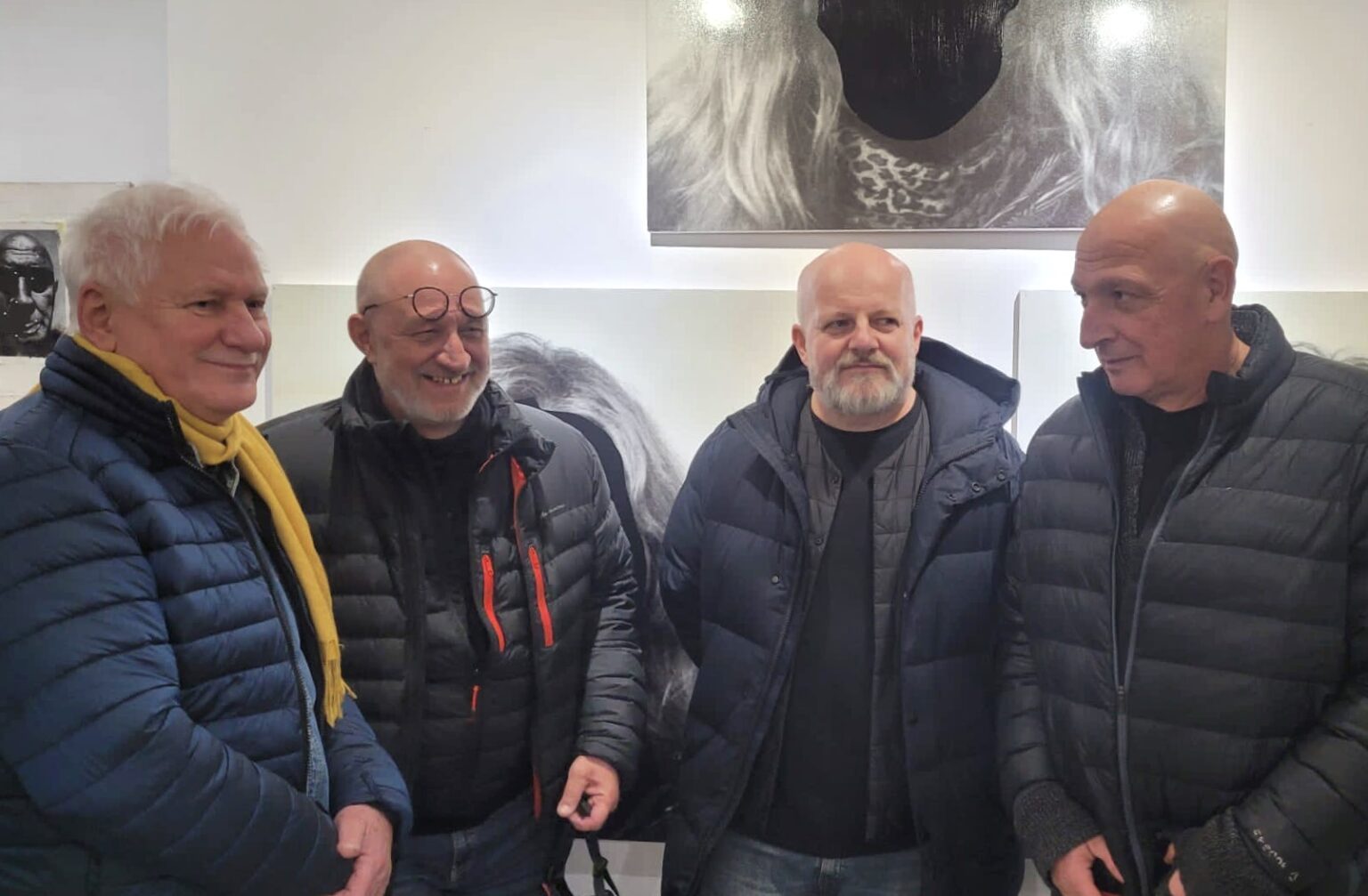 Czterech mężczyzn w puchowych kurtkach, obrazy w tle