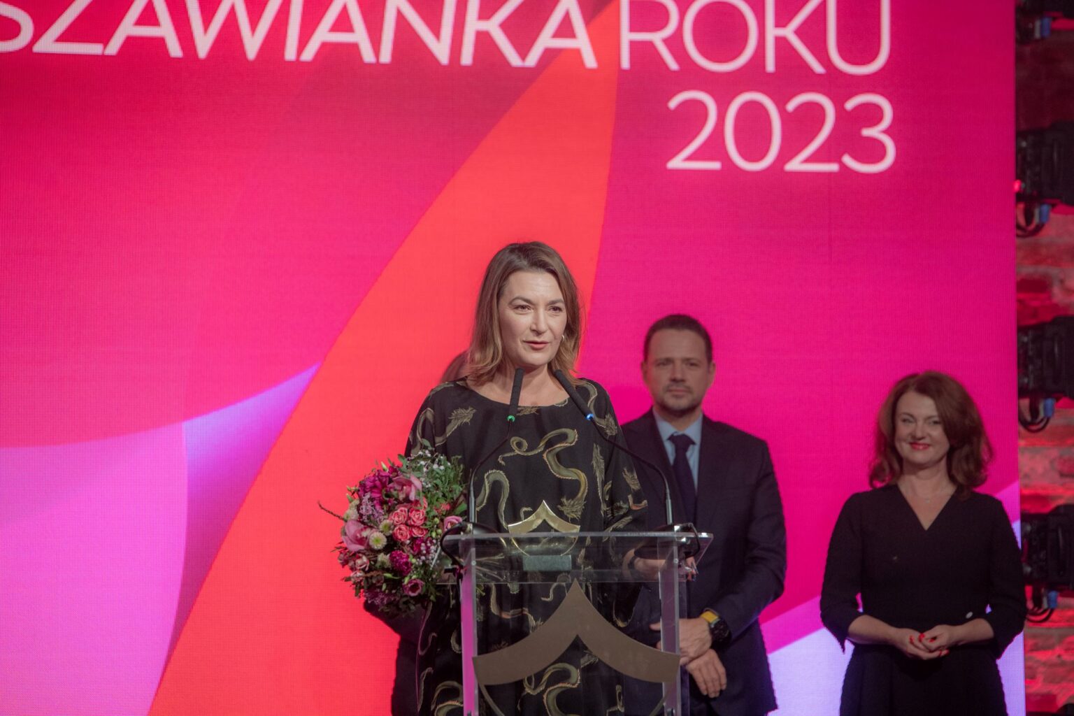 Kobieta przy mikrofonie. Osoby w tle