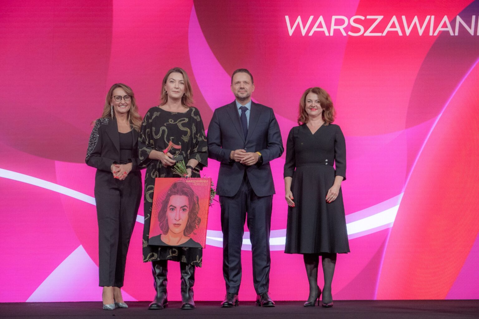 Cztery osoby na scenie. Kobieta trzyma obraz ze swoja podobizną