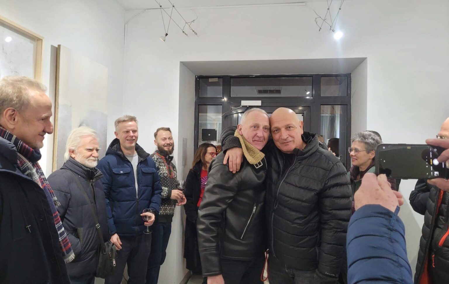 Dwaj mężczyźni - jeden obejmuje drugiego ramieniem. Wokół inni ludzie