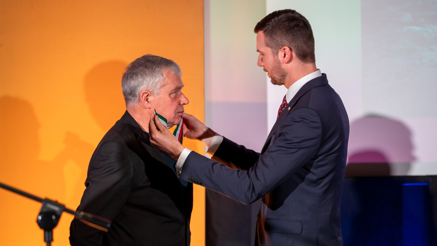 Dwaj mężczyźni, Jeden w uroczystym geście zakłada drugiemu medal