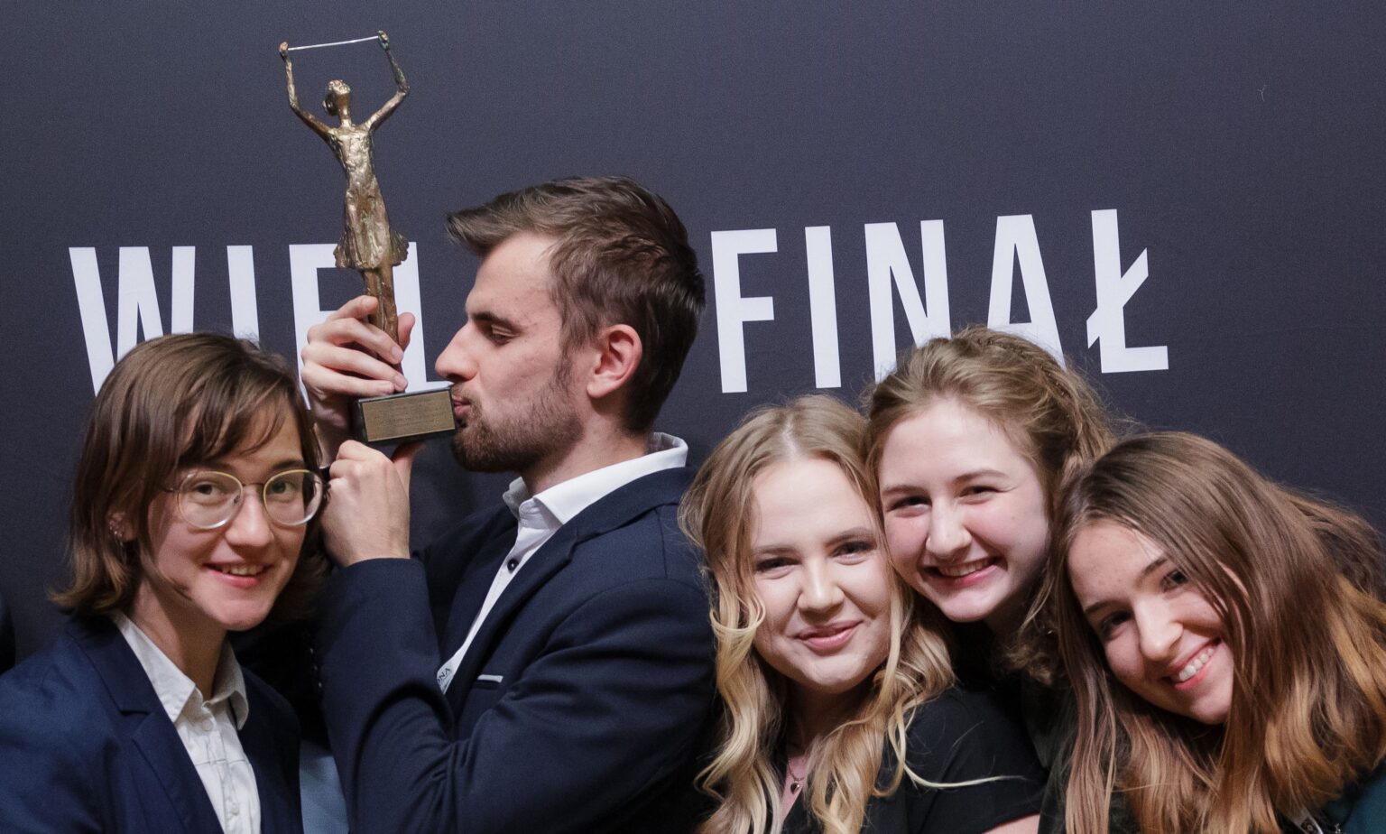 Uśmiechnięte osoby. Młody mężczyzna trzyma statuetkę w geście zwycięstwa