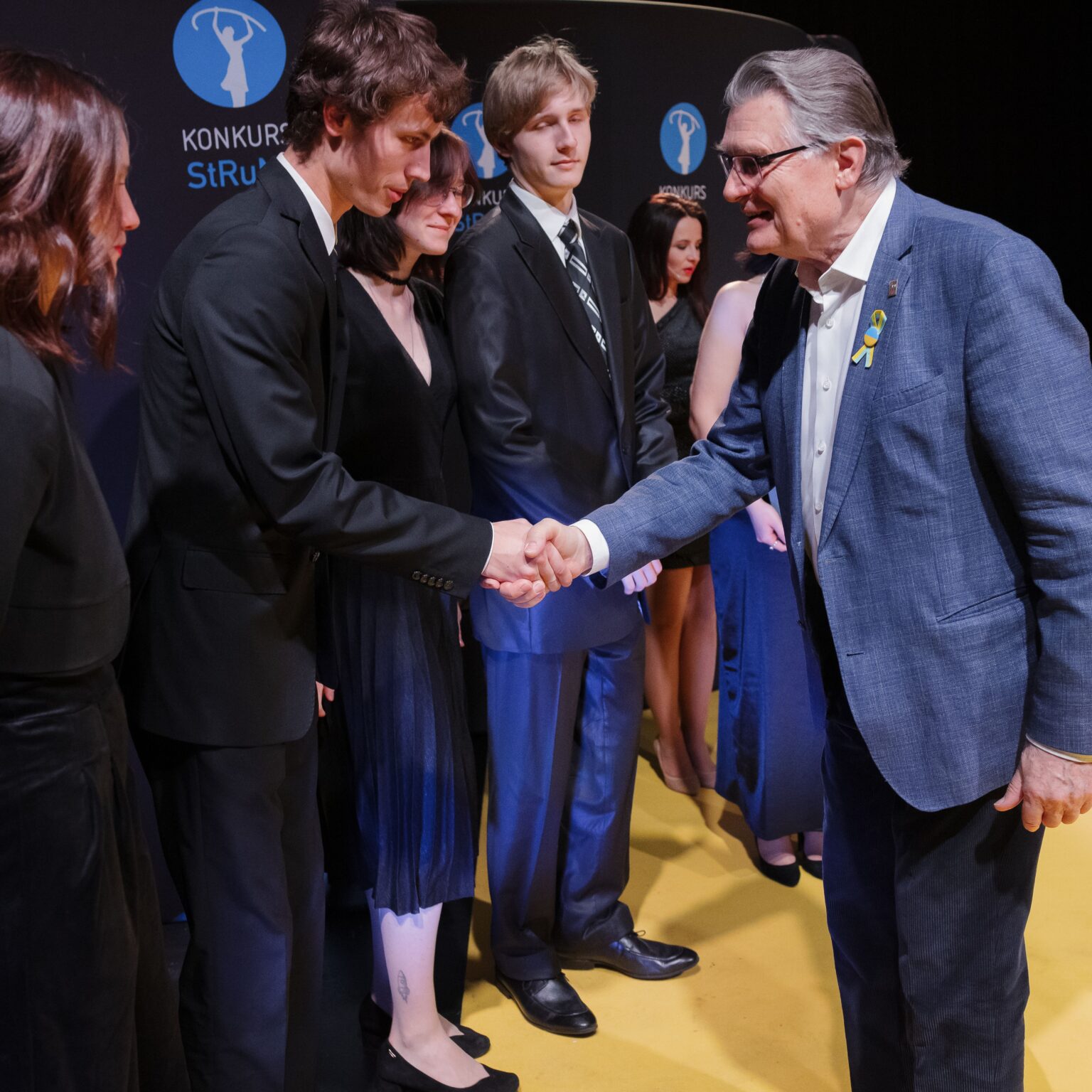 Dwaj mężczyźni podają sobie ręce w geście gratulacji. Osoby w tle