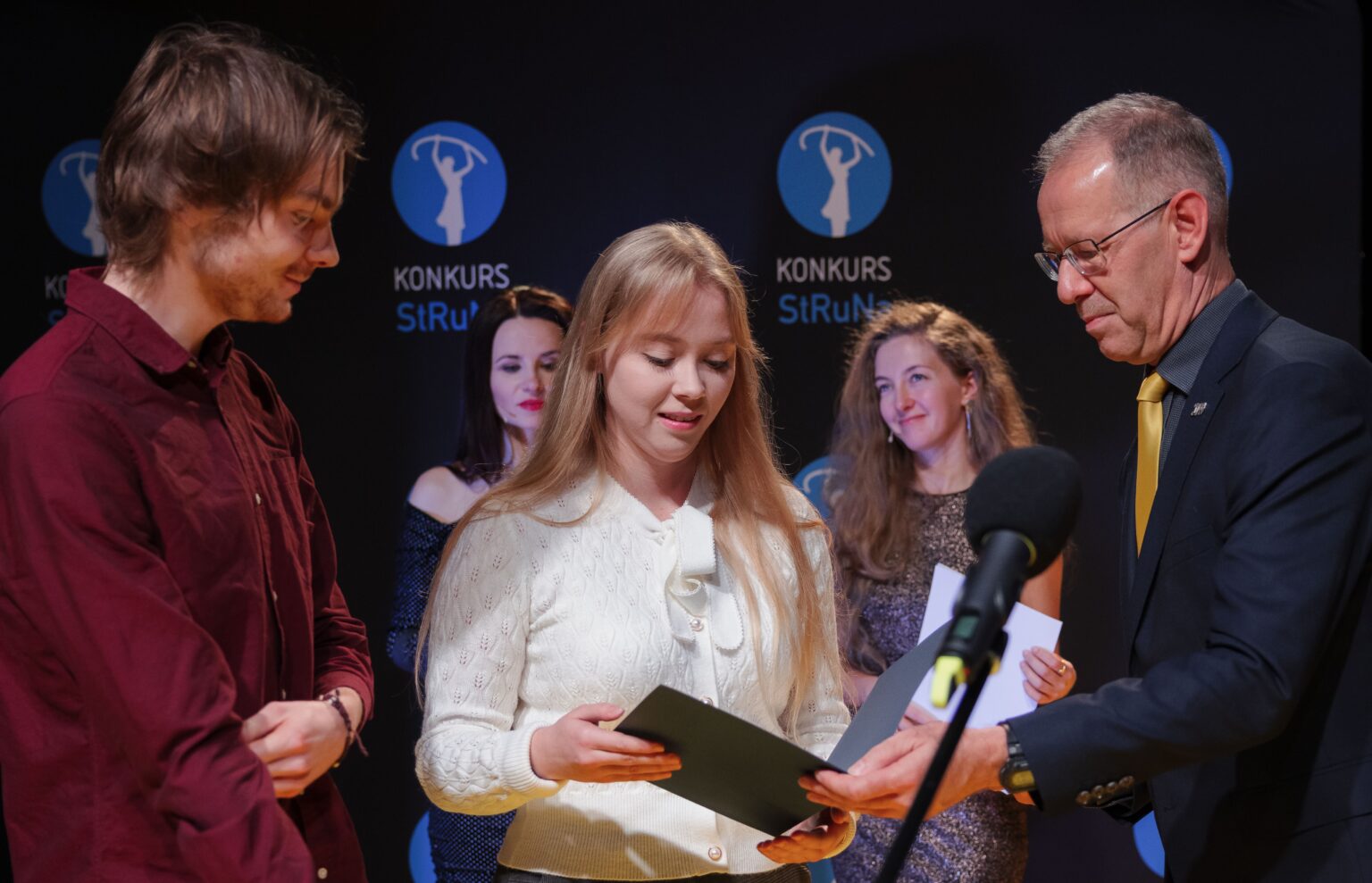 Kilka osób. po środku młoda kobieta trzyma dyplom