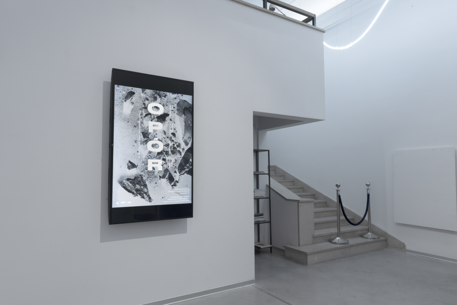 Plakat promujący wystawę na białej ścianie.