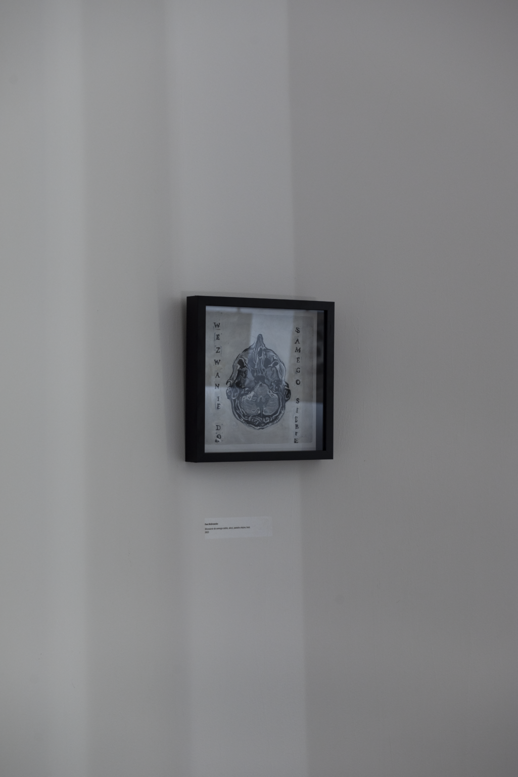 Praca w czarnej ramce wisząca na białej ścianie.