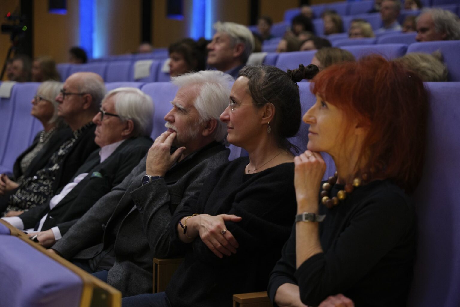 Kobiety i mężczyźni siędzą na siedzeniach patrząc na scenę.