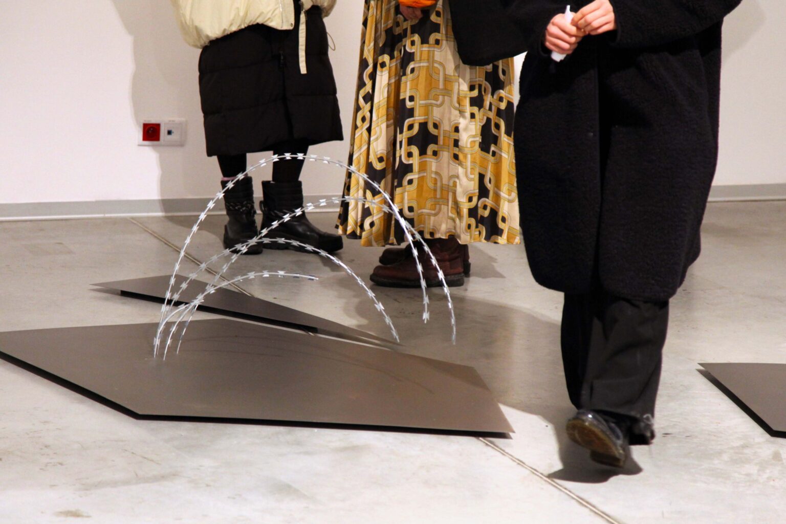 Eksponat z drutu na podłodze. Nogi osób zwiedzających na drugim planie