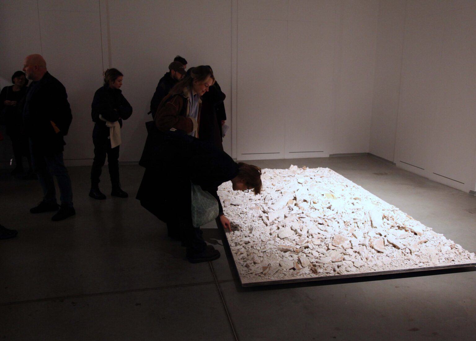 Duża grupa osób w przestrzeni galerii. Eksponat z wysypanych białych kamieni na podłodze