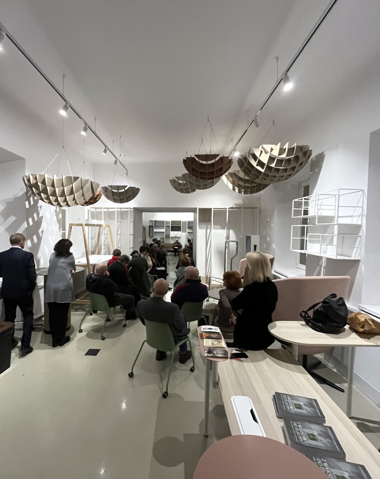 Grupa osób przysłuchuje sie rozmowie trzeb osób siedzących w fotelach