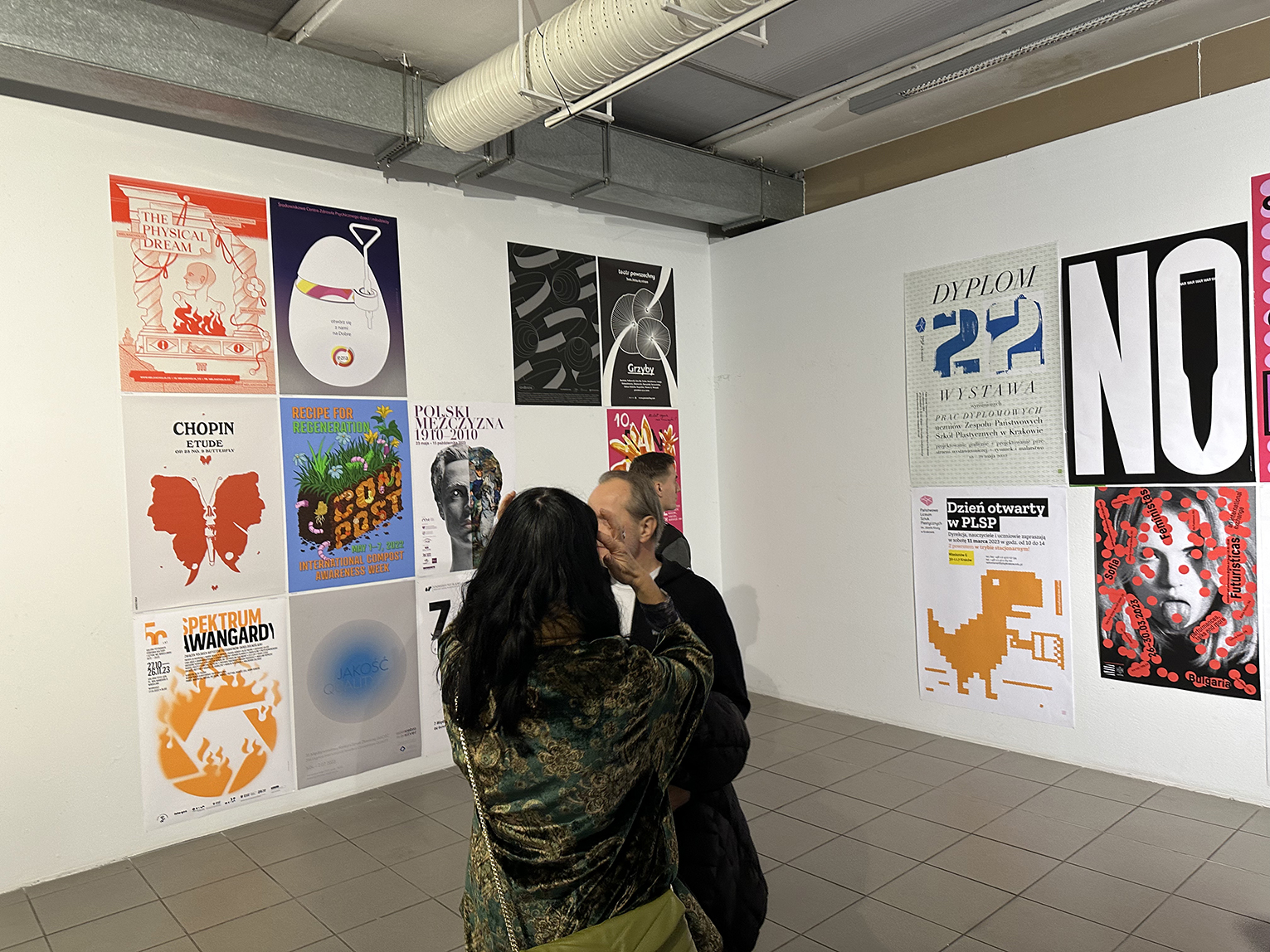 Dwie osoby podziwiające plakaty na wystawie.