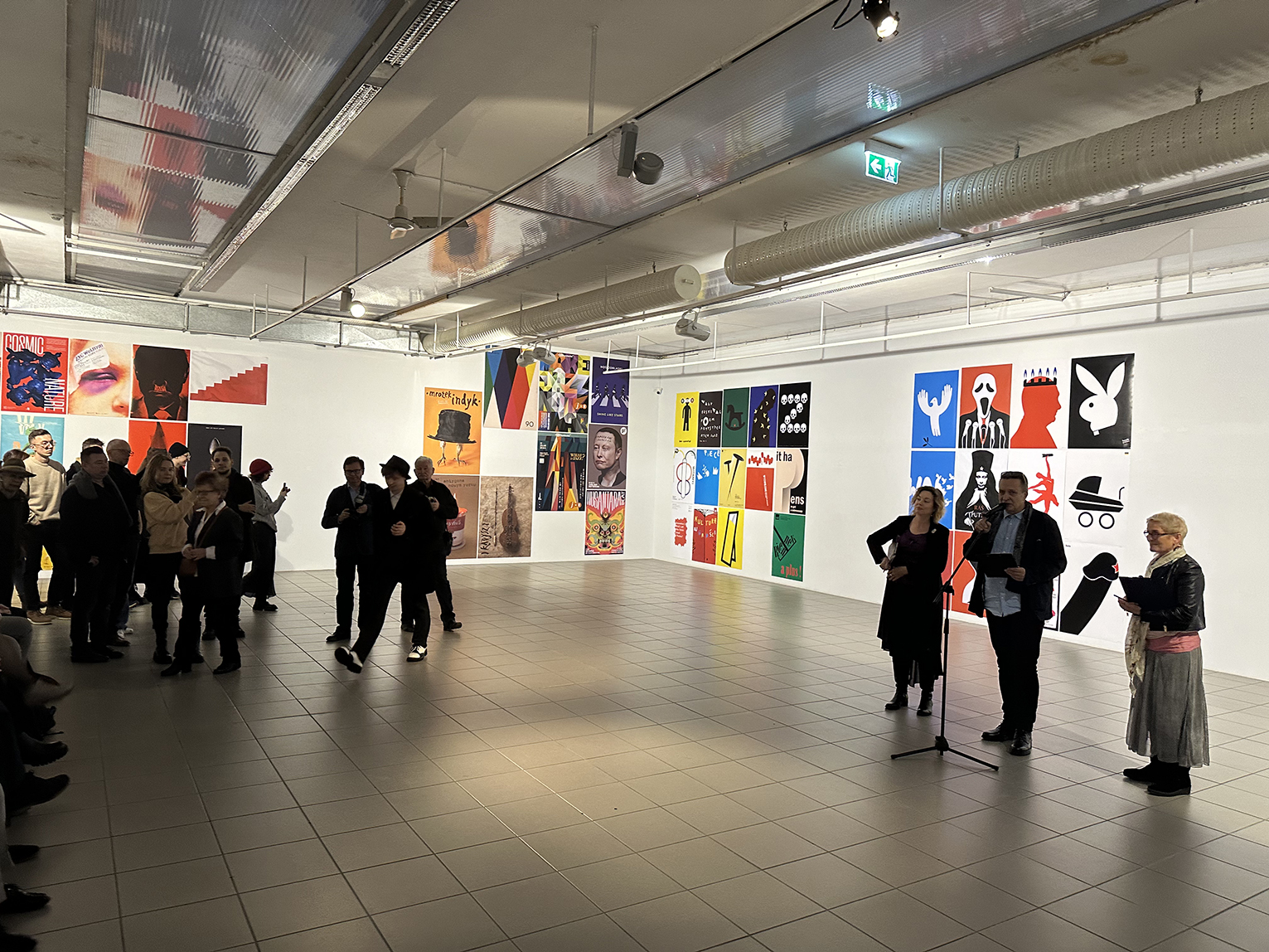 Grupa osób oglądająca plakaty na wystawie.