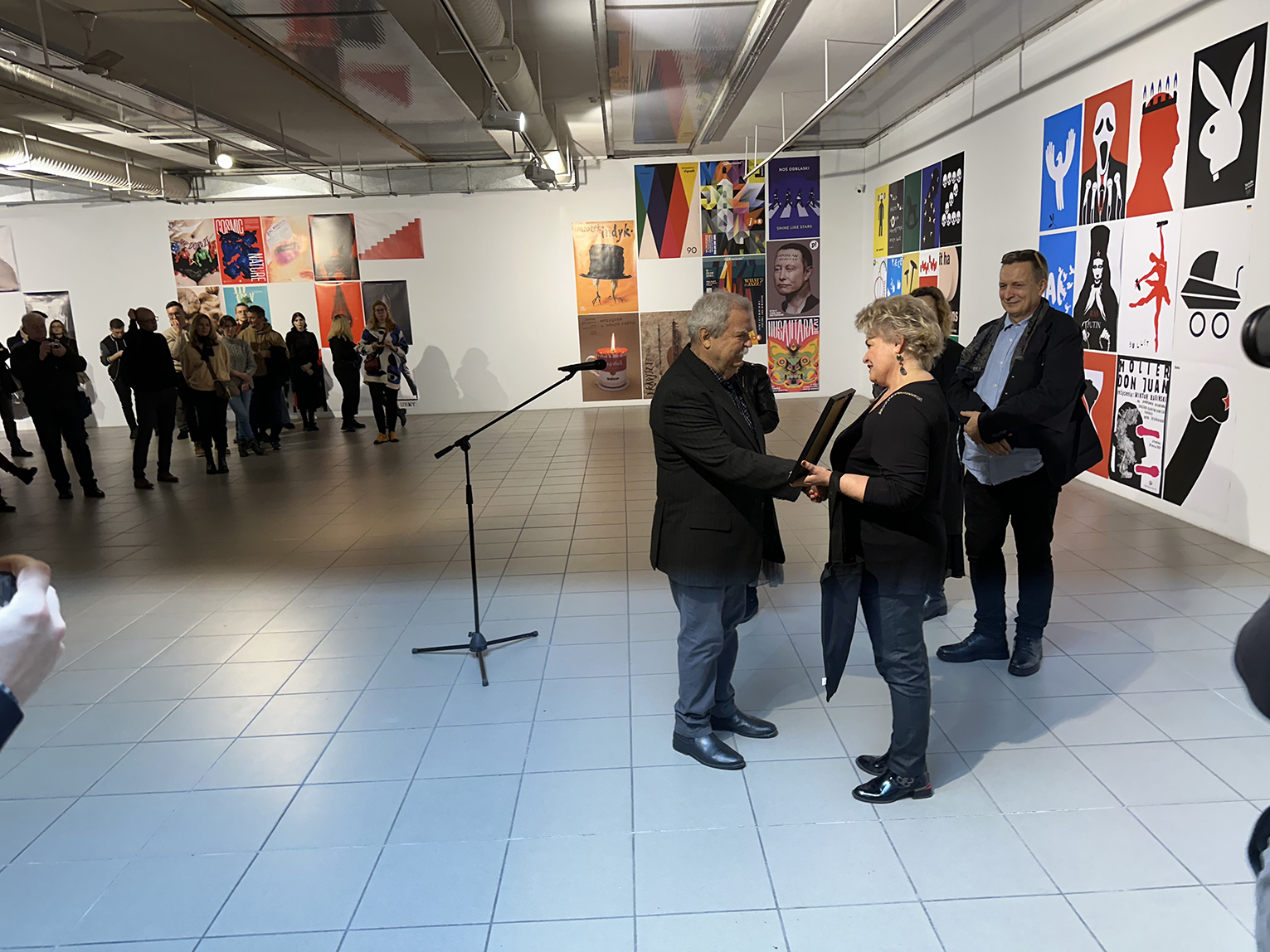 Kobieta i mężczyzna podający sobie dłoń. W tle plakaty.