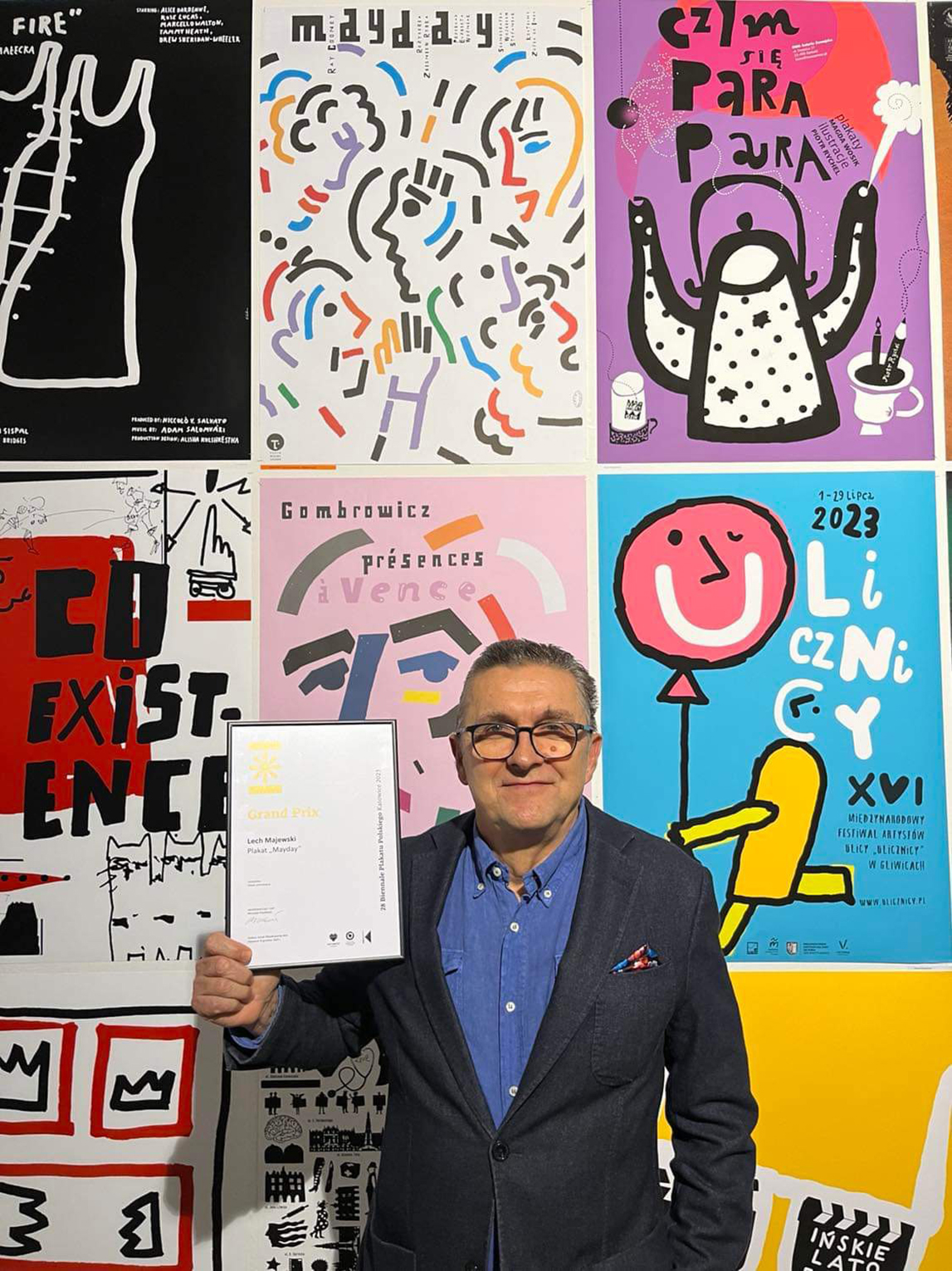 Mężczyzna trzymający w ręku nagrodę. W tle wiszące plakaty.