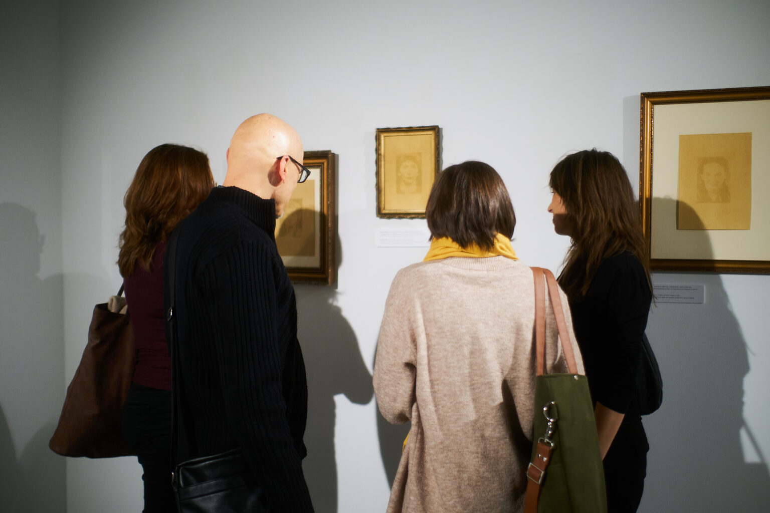 Osoby stoją tyłem, przyglądają się pracom na ścianie