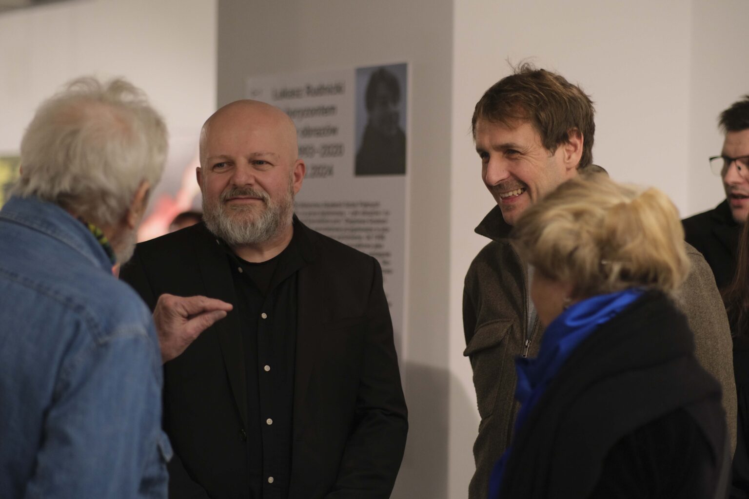 Cztery osoby rozmawiają. Wystawa w tle