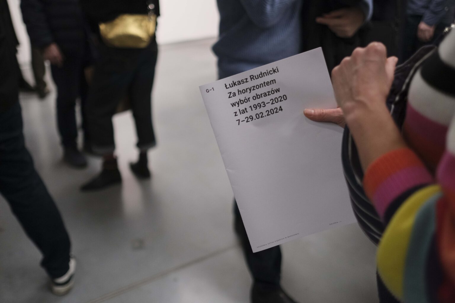 Folder z nazwą wystawy w dłoni osoby zwiedzającej