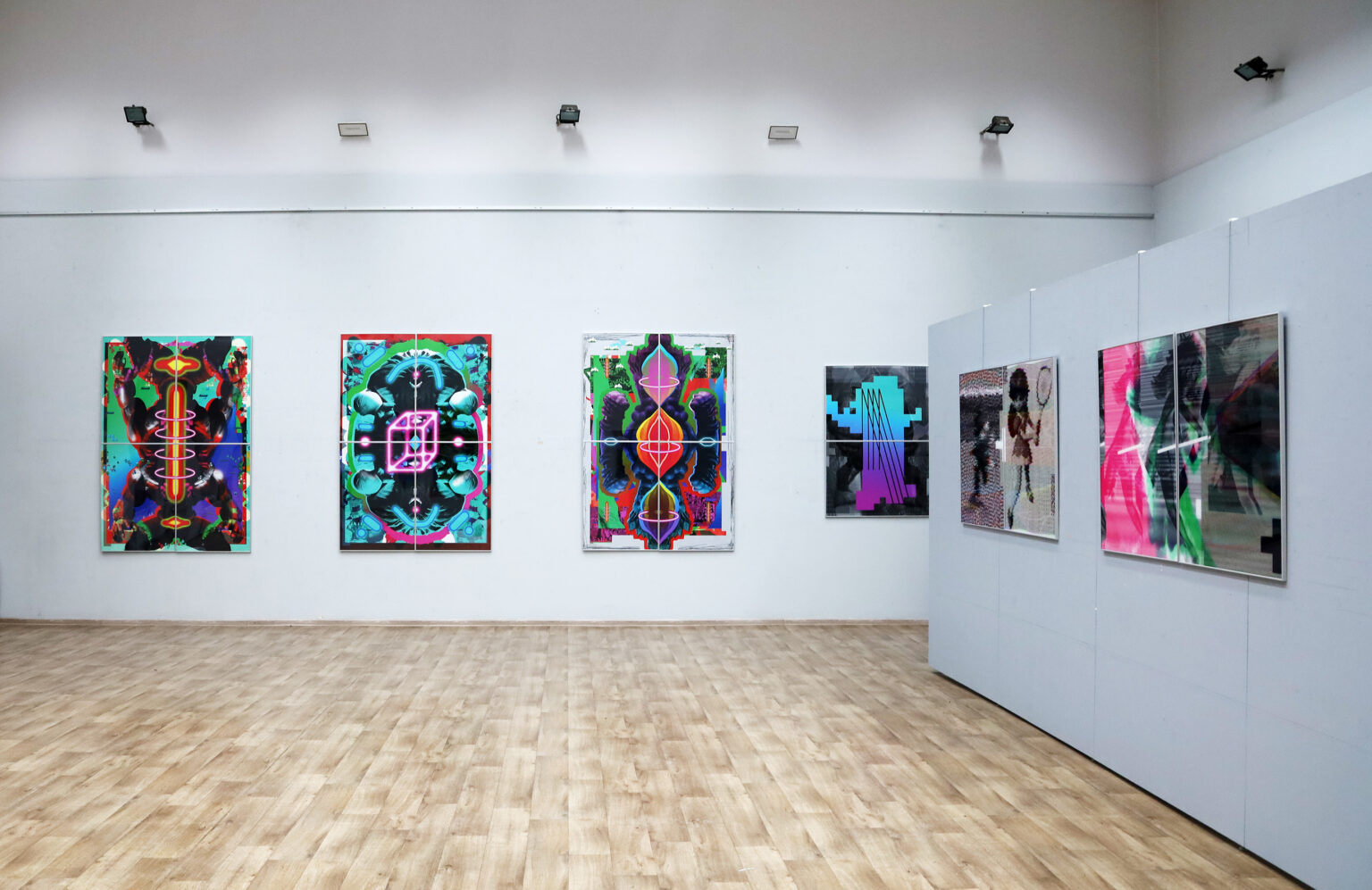 Wystawa kolorowych prac wiszących na białej ścianie.