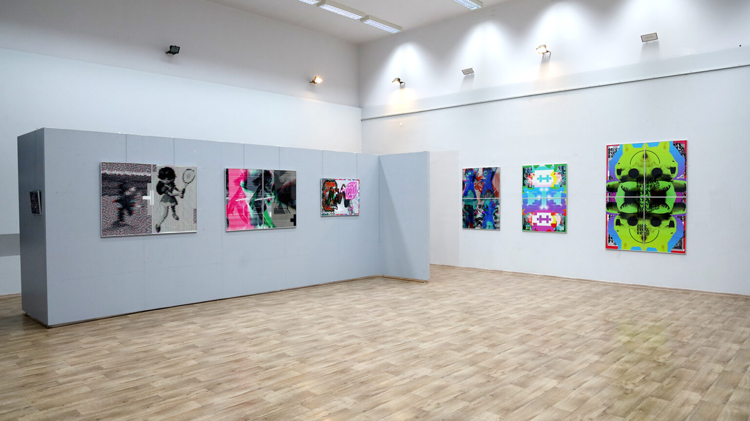 Widok całej sali wystawowej. Na białych ścianach kolorowe prace.