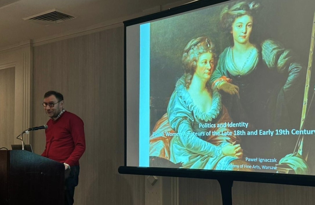 Mężczyzna na mównicy. Po prawej ekran z prezentacją