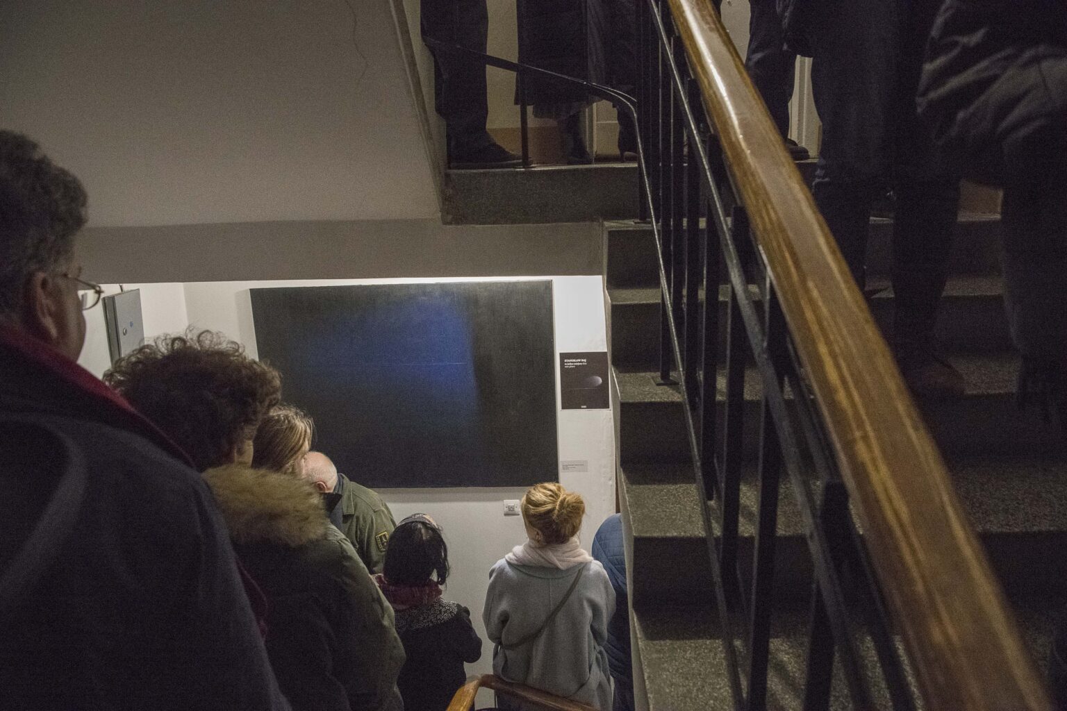 Grupa osób stojących na klatce schodowej, obrazy w tle