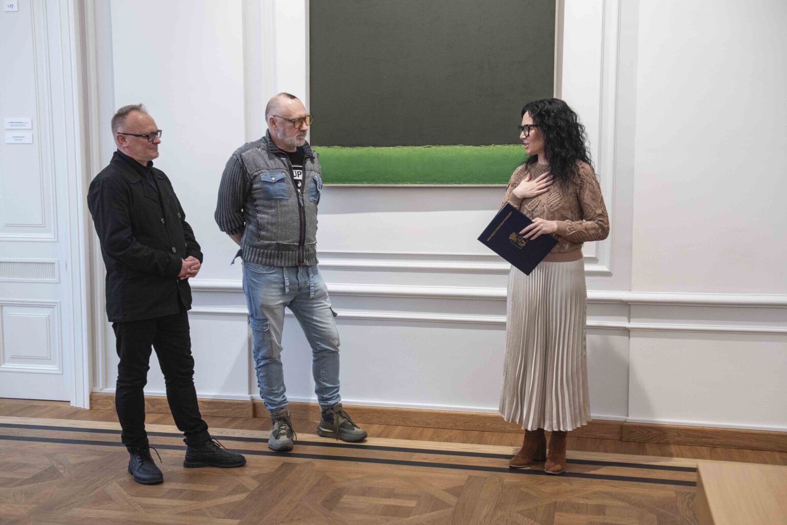 Dwaj mężczyźni i kobieta na tle obrazu w zielonych barwach