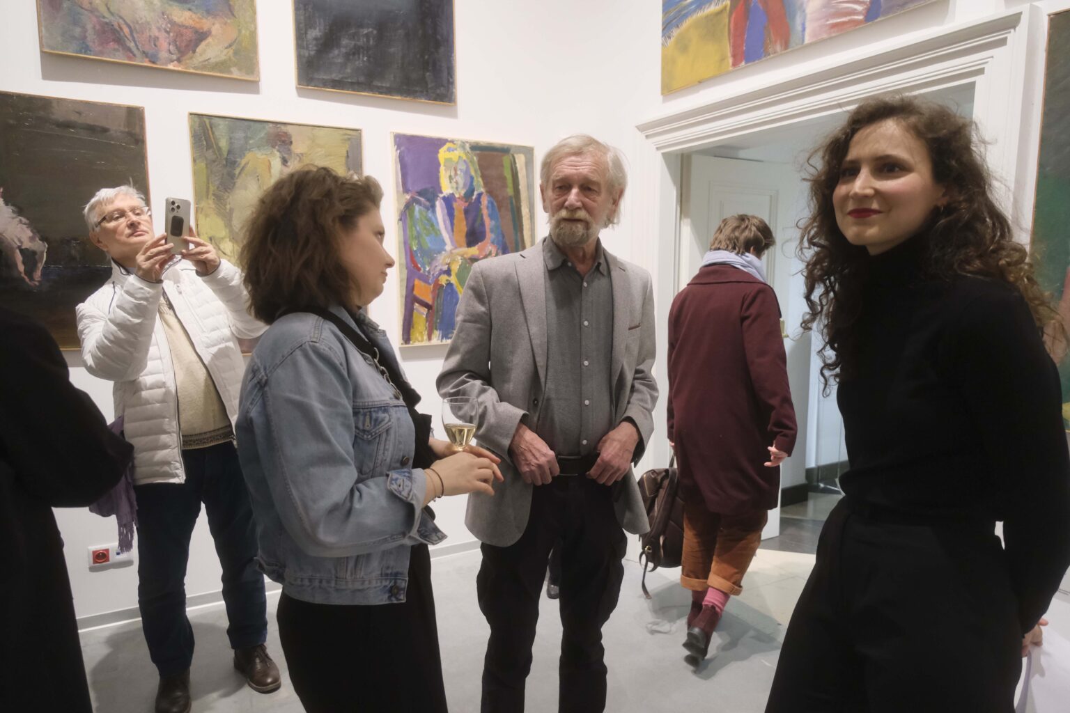 Trzy osoby rozmawiają. Wystawa w tle