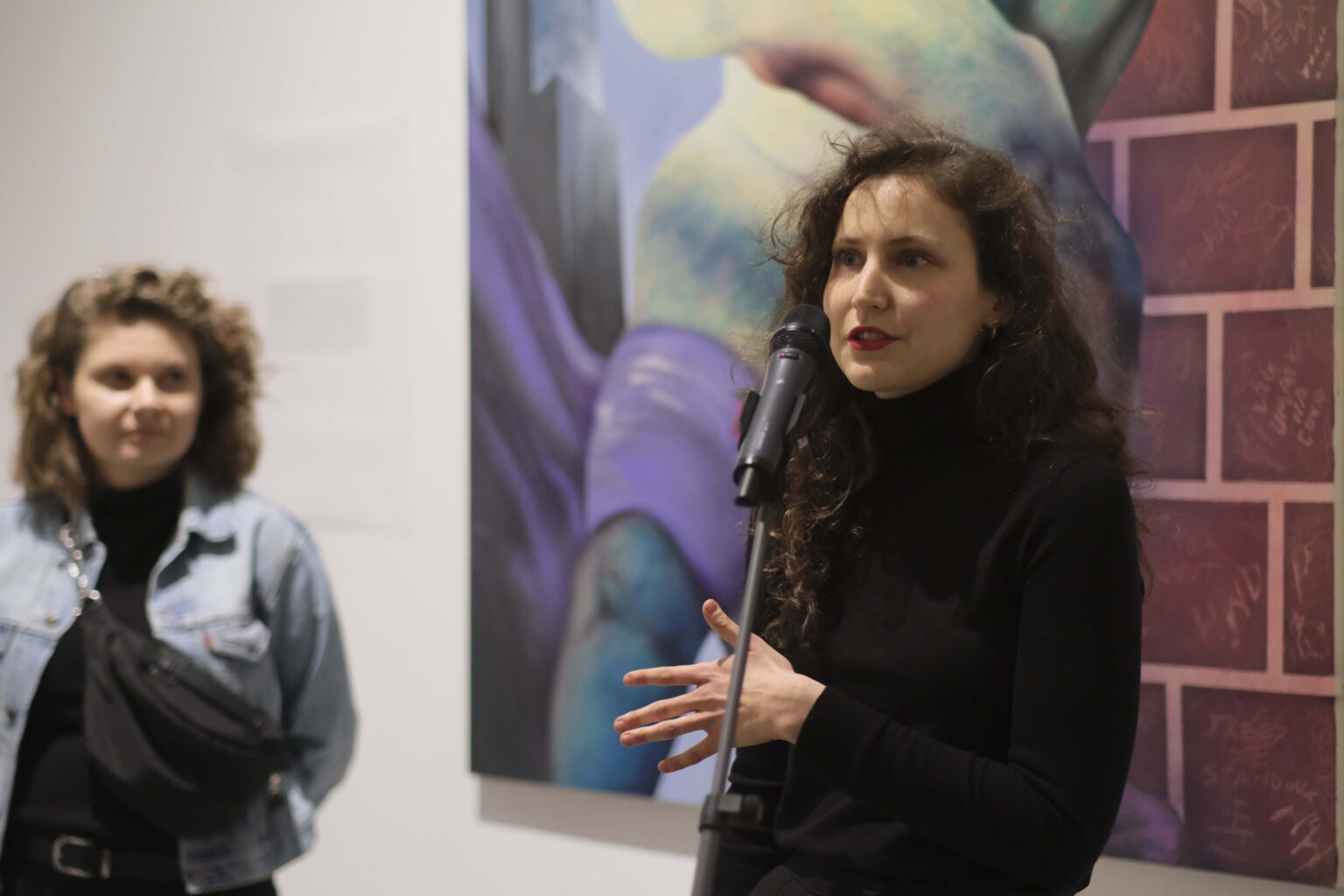 Młoda kobieta przy mikrofonie. W tle obraz.