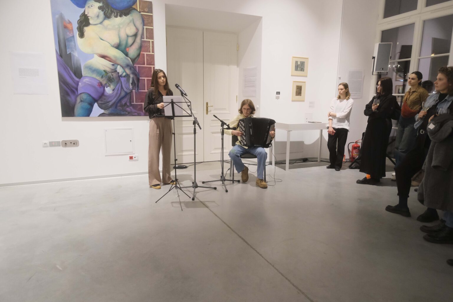 W przestrzeni galerii: kobieta stoi przy mikrofonie, mężczyzna gra na akordeonie