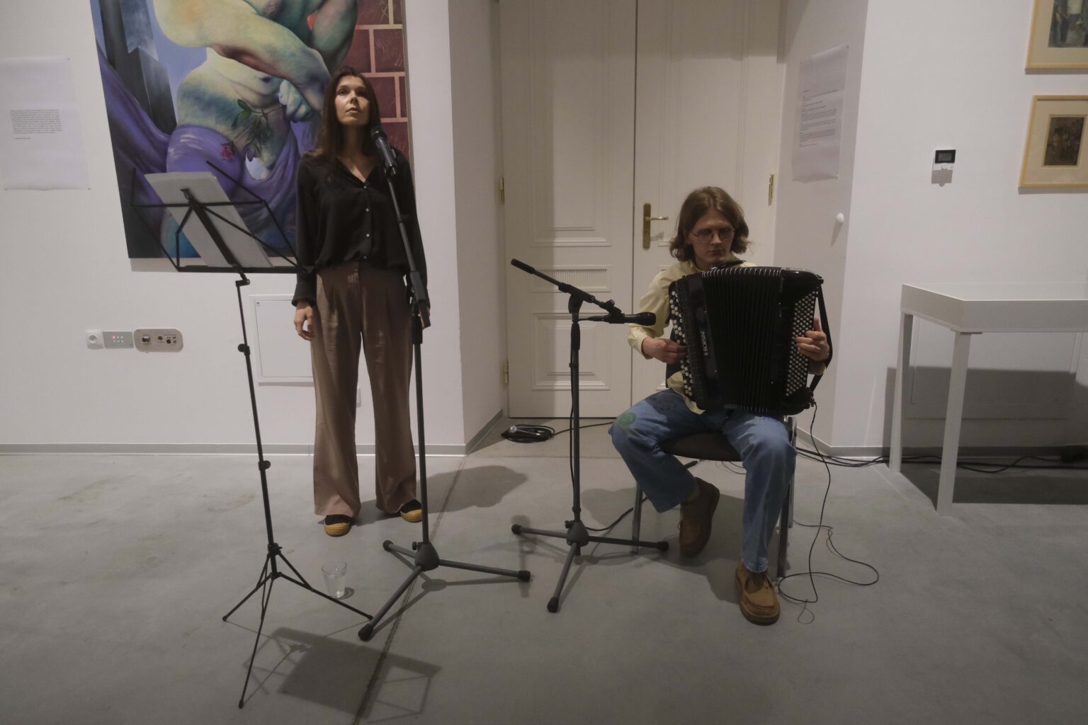 Młoda kobieta stoi przy mikrofonie, mężczyzna gra na akordeonie