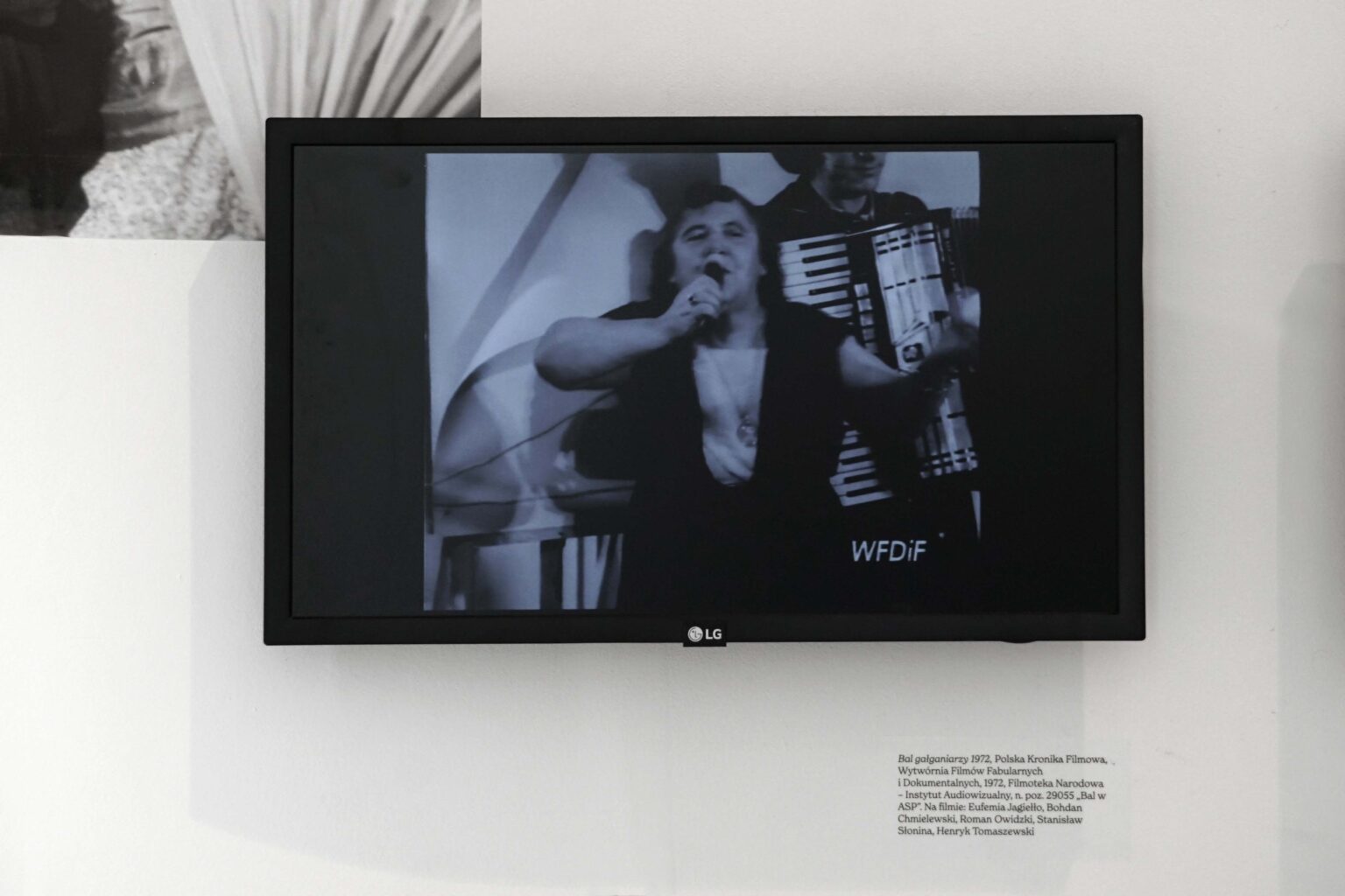 Zbliżenie na monitor prezentujący klatkę z filmu przedstawiającą kobietę śpiewającą do mikrofonu