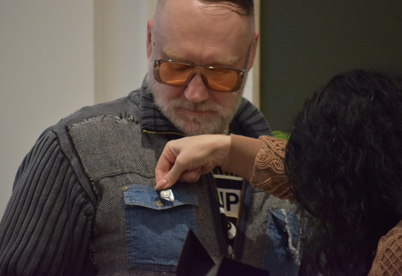 Kobieta (tyłem) przypina do klapy kurtki mężczyzny odznakę