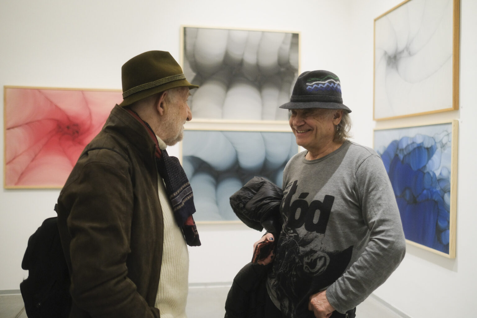 Dwaj mężczyźni w kapeluszach rozmwiają w przestrzeni galerii