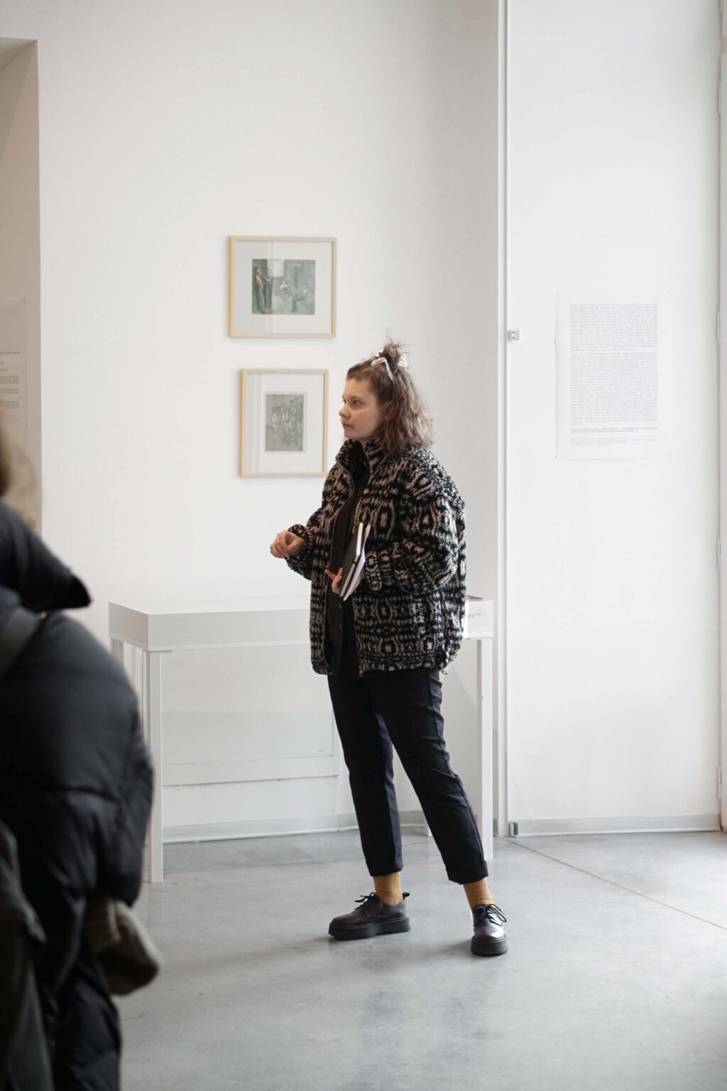 Kobieta mówi do zebranych osób, wystawa w tle