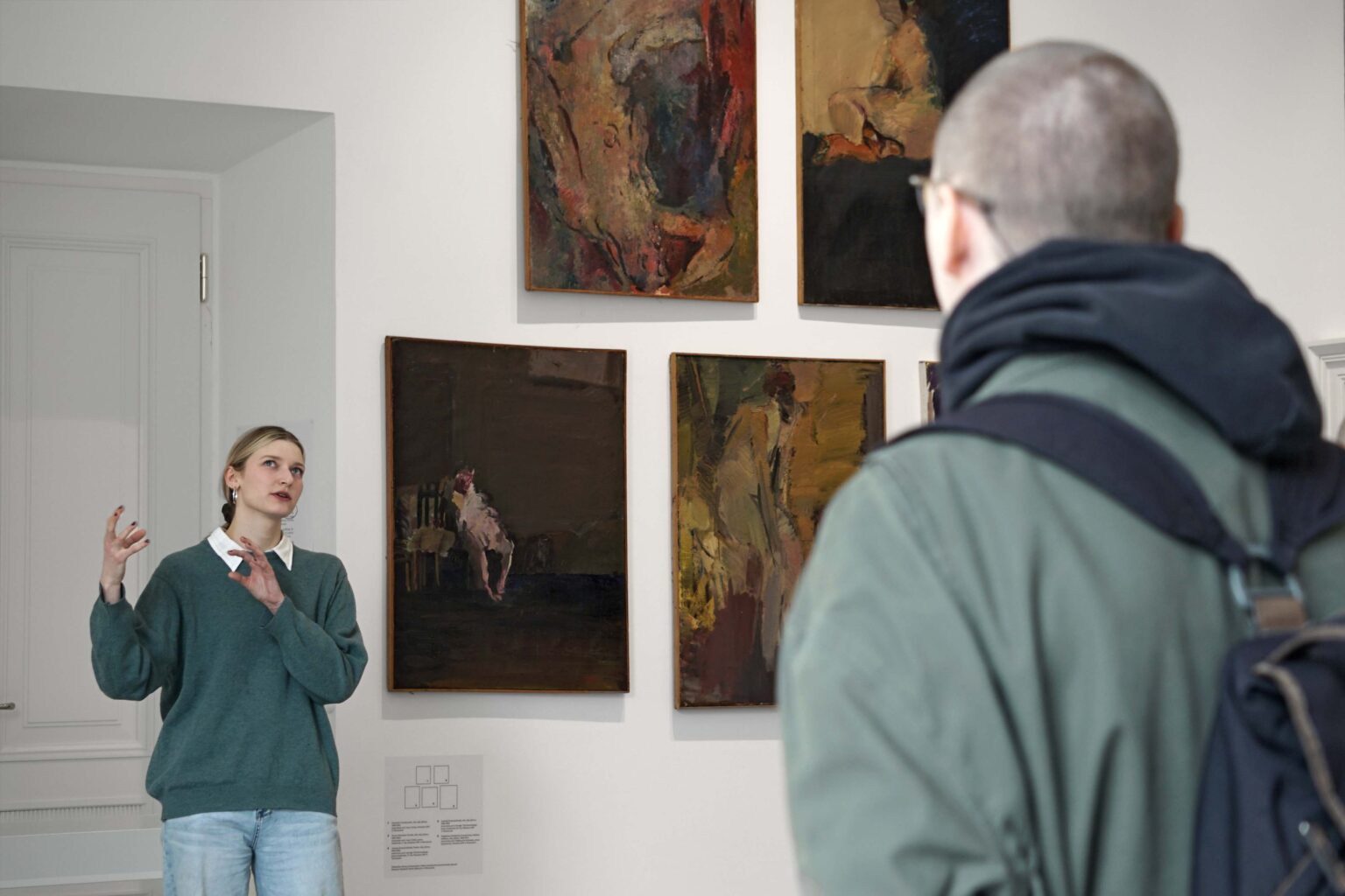 Kobieta w okularach mówi do słuchających osób, w tle wystawa