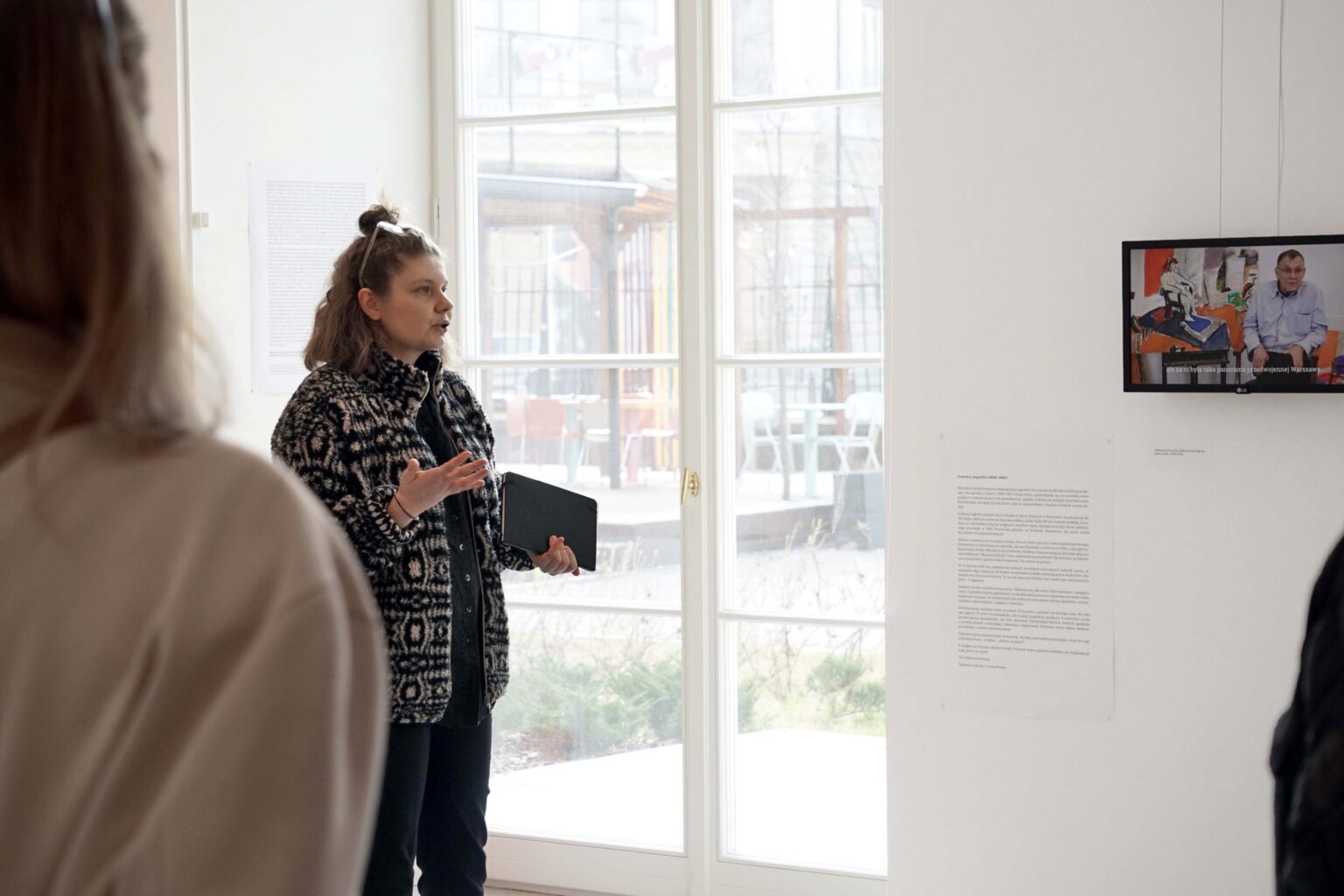 Kobieta tłumaczy coś zabranym osobom, w tle okno