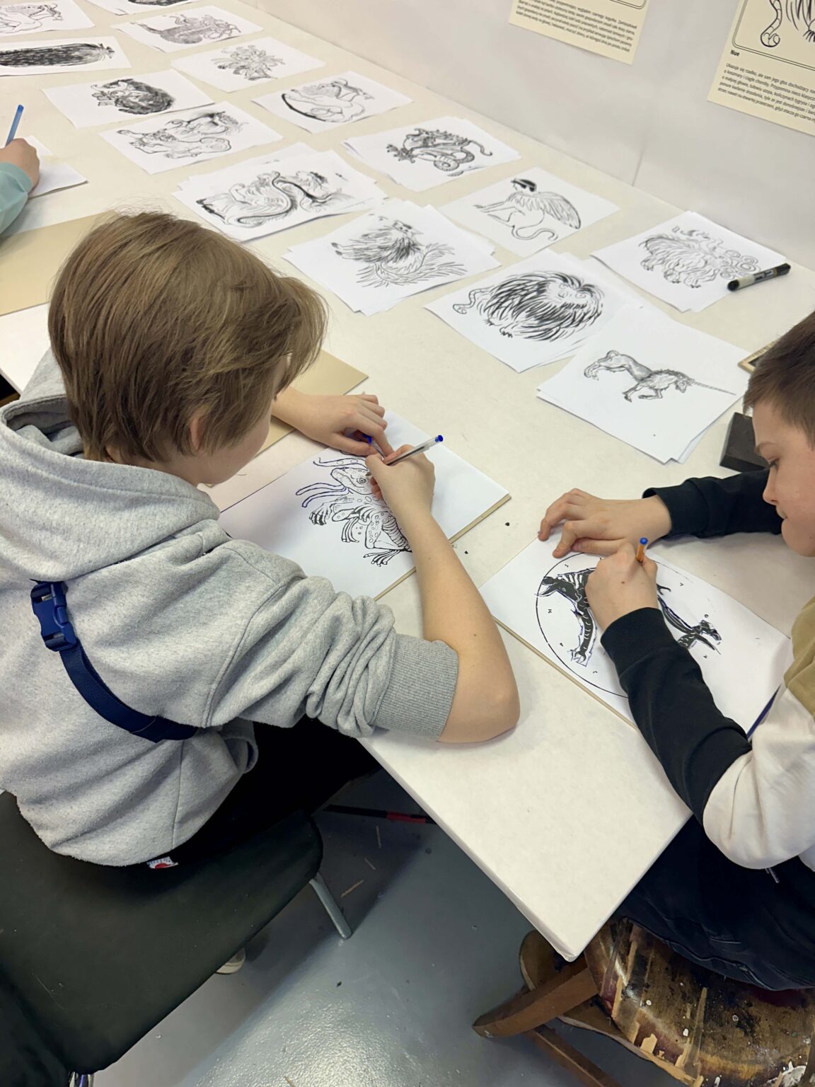 Grupa dzieci przy dużym stole podczas warsztatów. Na stole przybory do rysowania