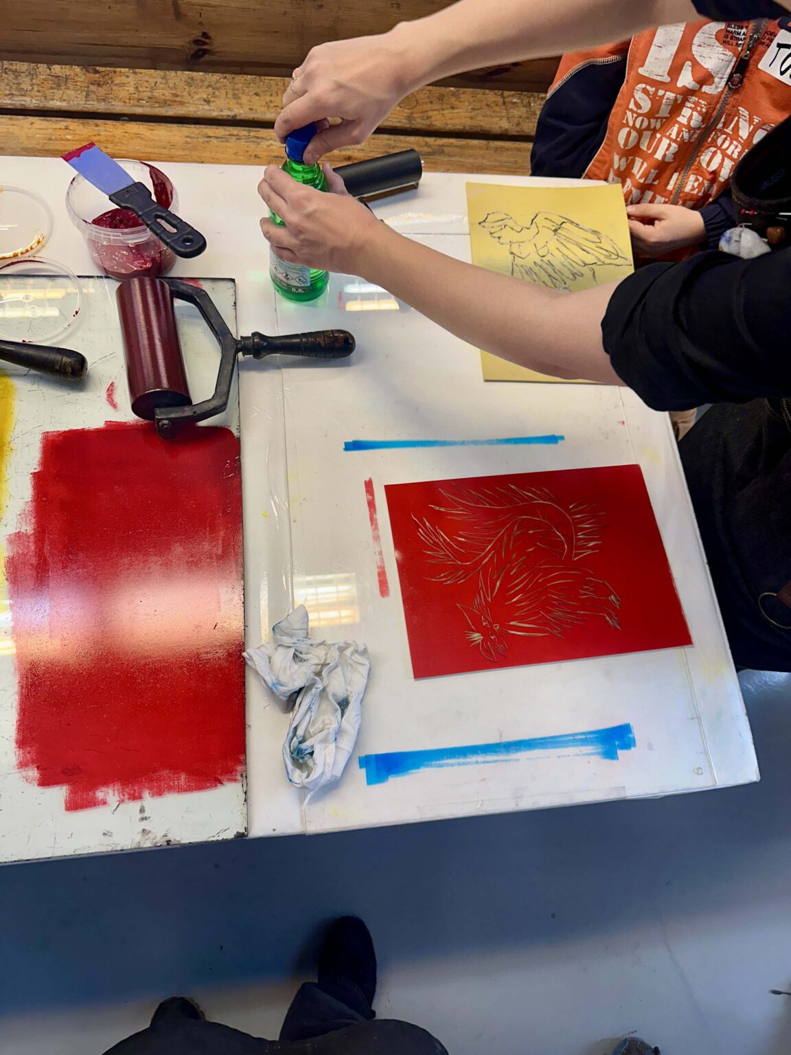 Grupa dzieci przy dużym stole podczas warsztatów. Na stole przybory do rysowania