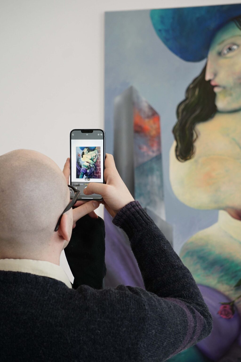 Mężczyzna (tyłem) robi zdjęcie smartfonem barwnemu obrazowi