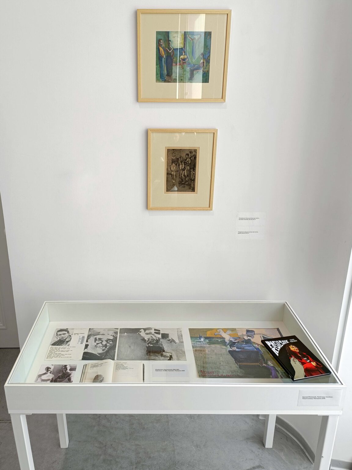 Dwa eksponaty w drewianych ramkach za szkłem, pod nimi biała gablota z innymi obiektami