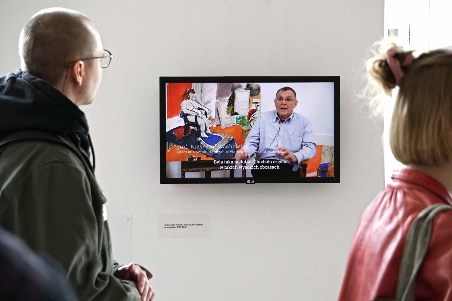Dwie osoby oglądaja film na ekranie powieszonym na ścianie galerii