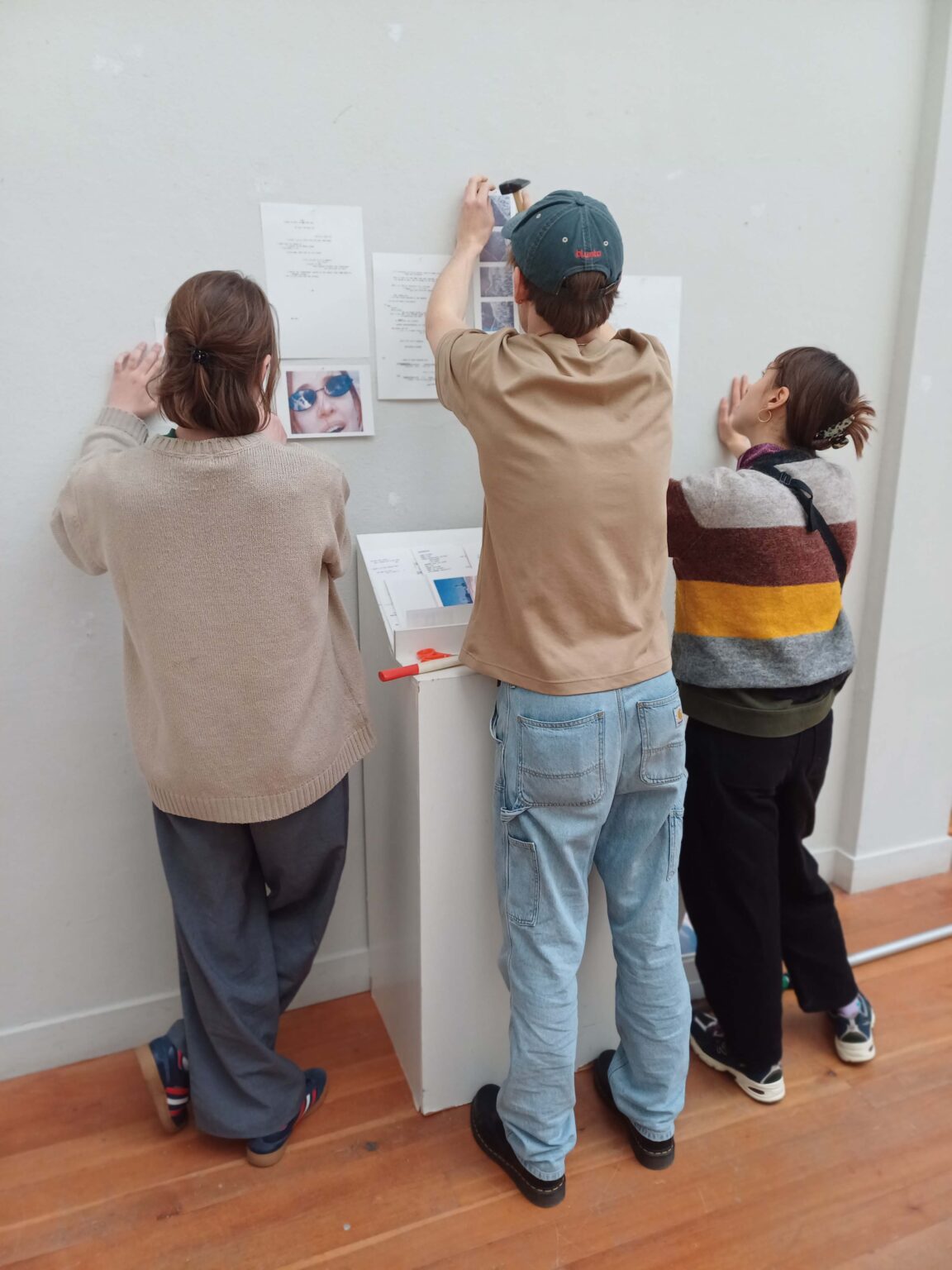 trzy osoby wieszają prace na ścianie