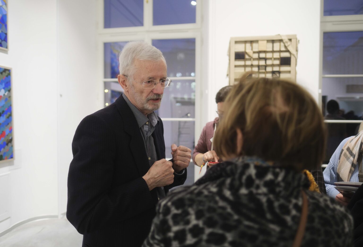 Mężczyzna rozmawia z kilkoma otaczającymi go osobami. Obraz w tle