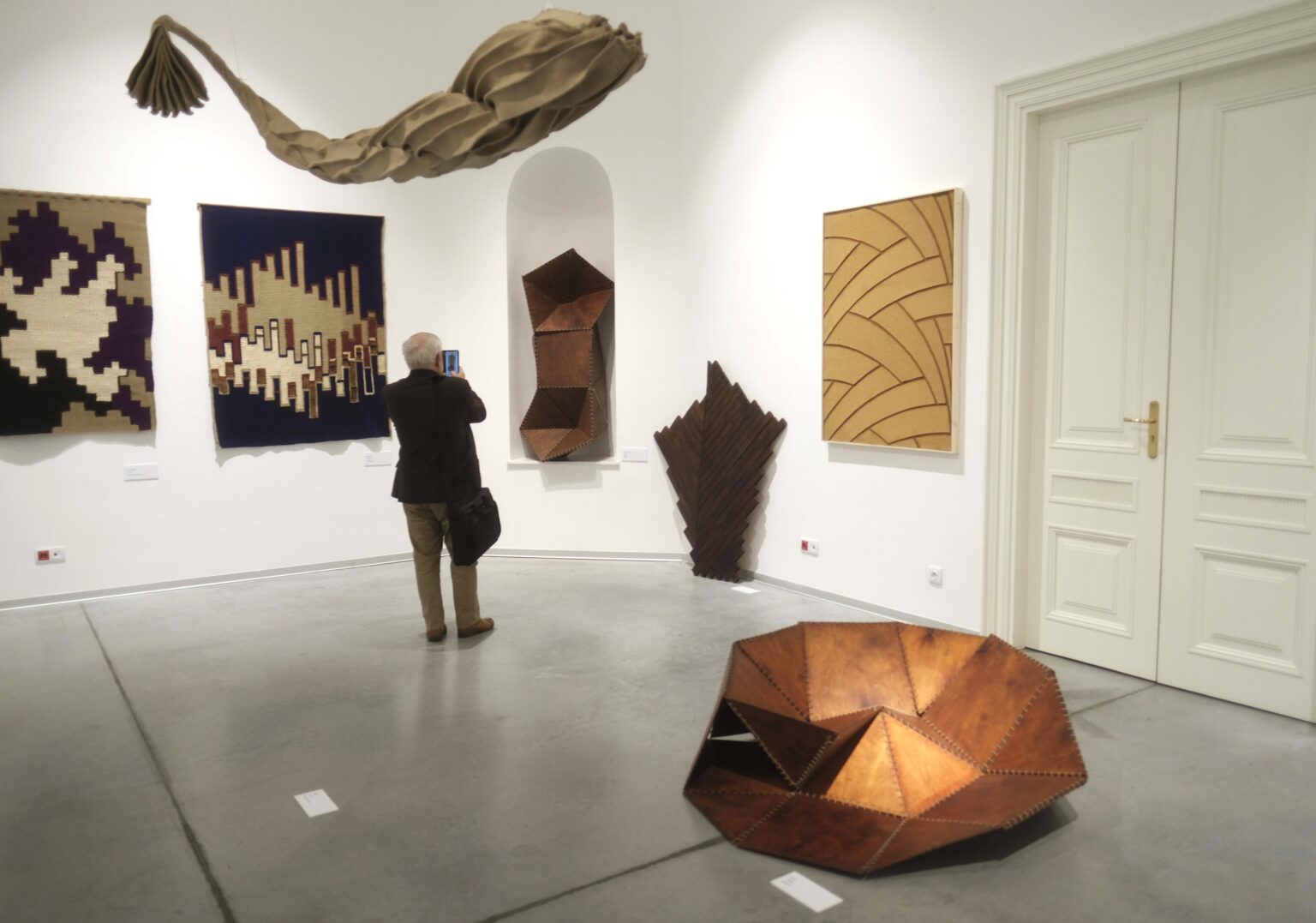 Zwiedzający w galerii. Obrazy na ścianach. Obiekty: na podłodze, pod ściana i podwieszony pod sufitem