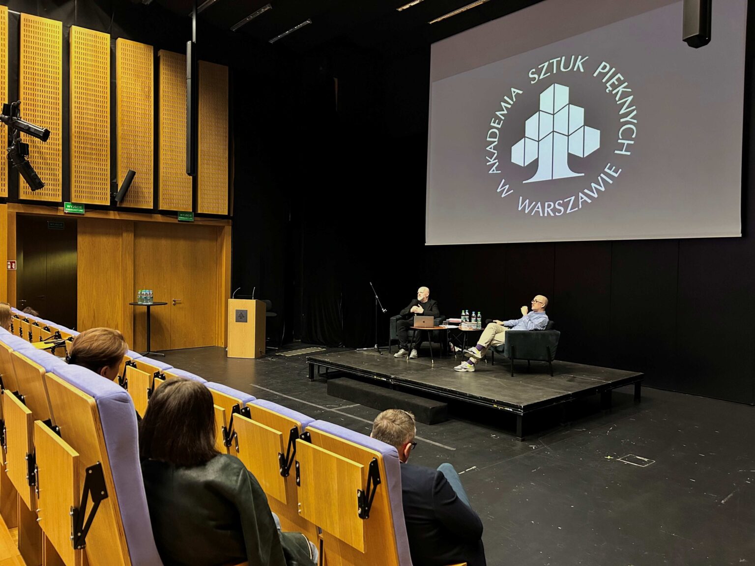 Dwie osoby siedzą na podwyższeniu i rozmawiają