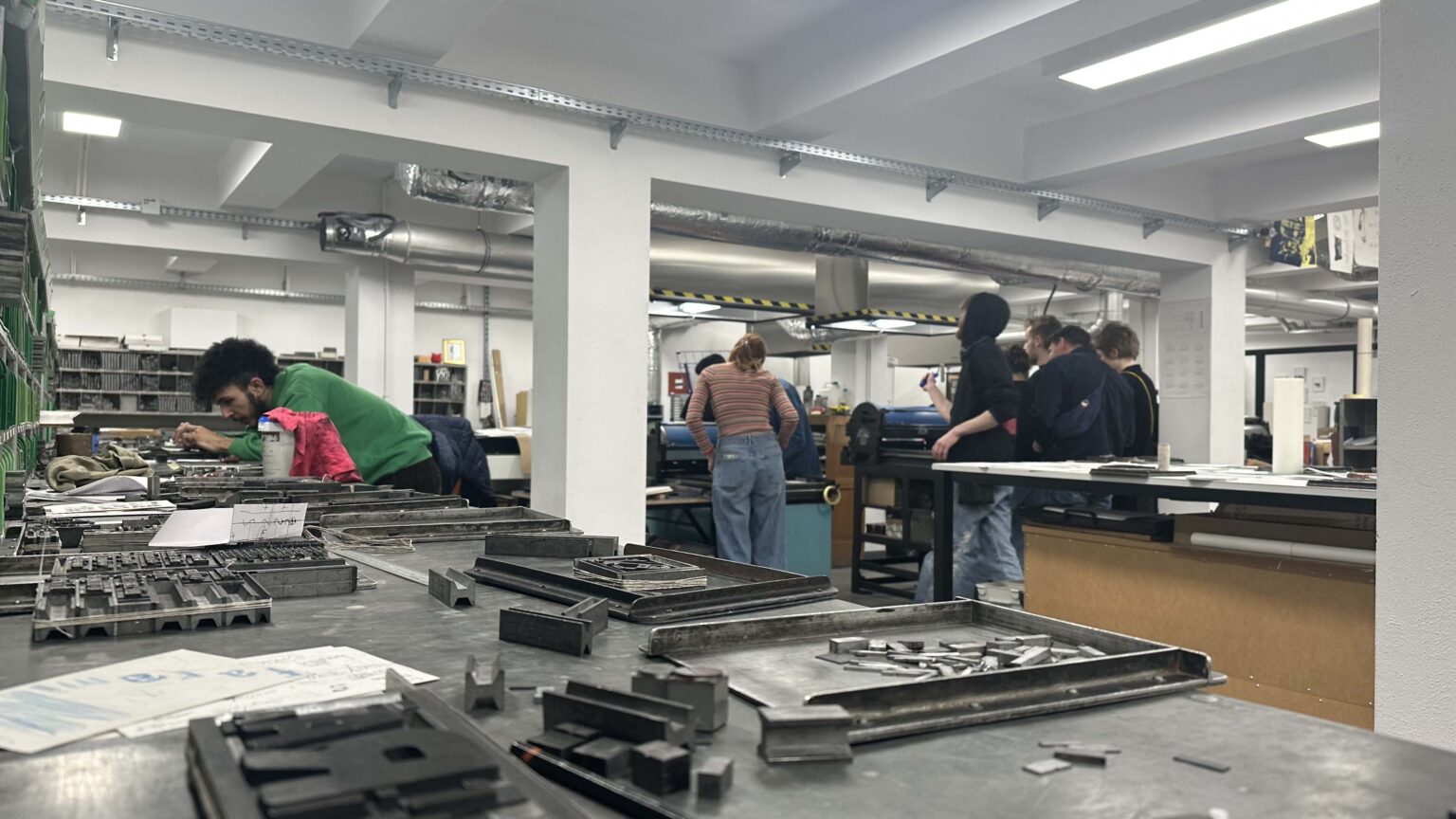 Widok pracowni zecerskiej. Osoby przy pracy w tle