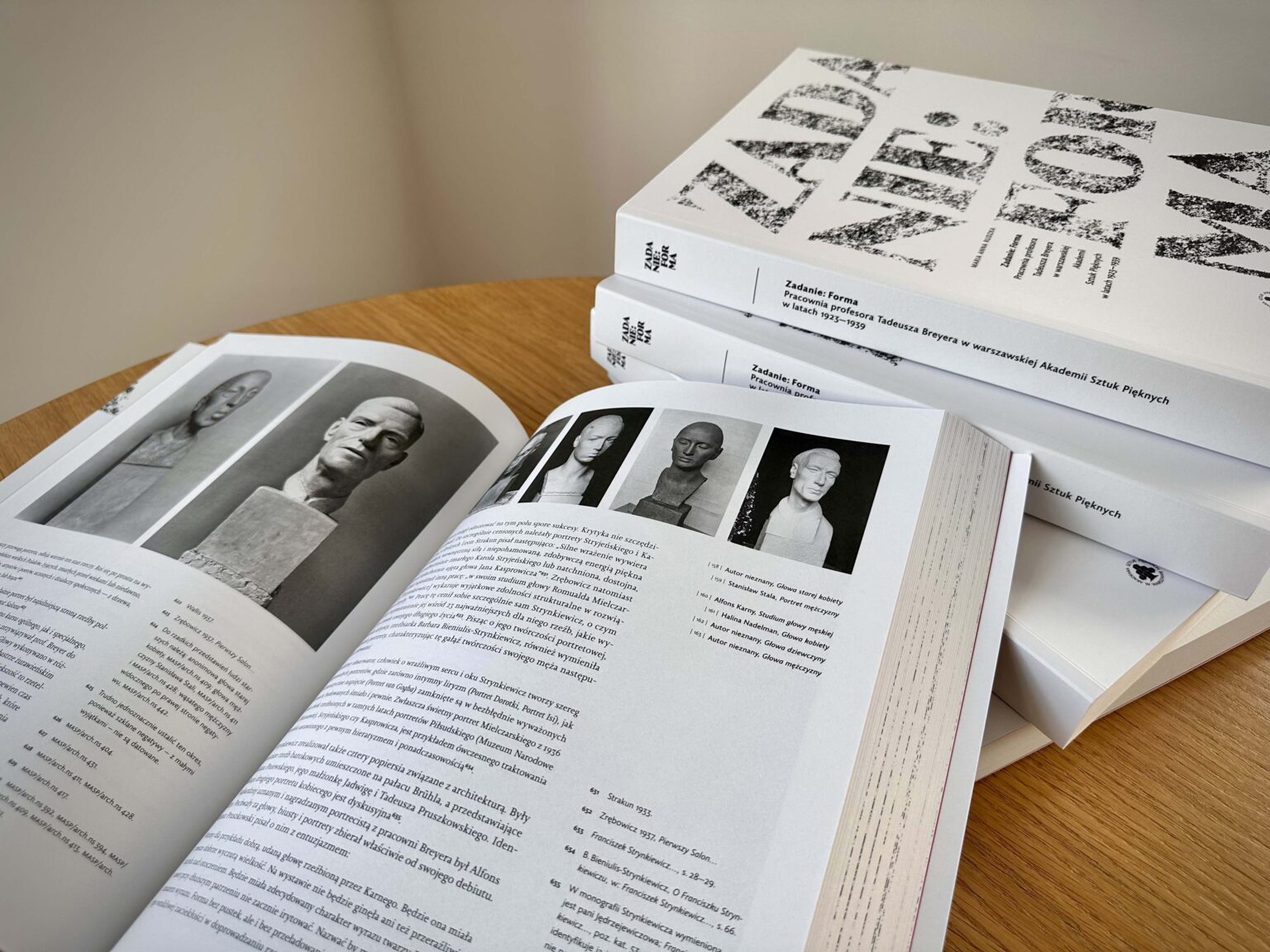 Otwarta książka na blacie stołu. Obok (po prawej stronie) 4 egzemplarze jeden na drugim