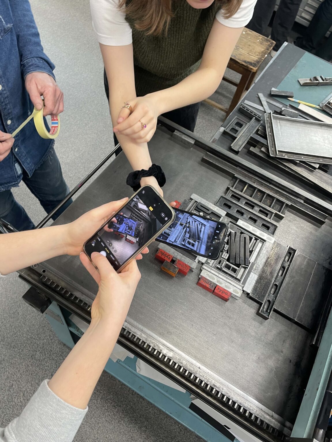 Ujęcie z góry: ręce trzymające smartfony fotografujące czcionki na stole zecerskim